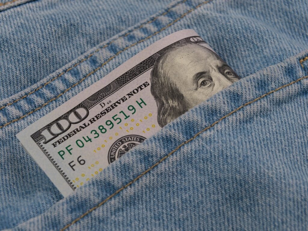 Close-up of a 100 dollar bill peeking from a blue denim pocket, symbolizing wealth and finance.