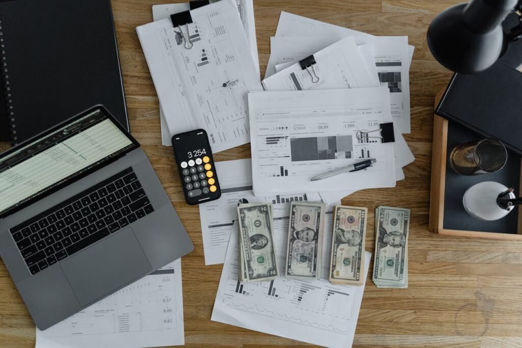 Overhead view of financial documents, cash, and technology on a wooden desk.