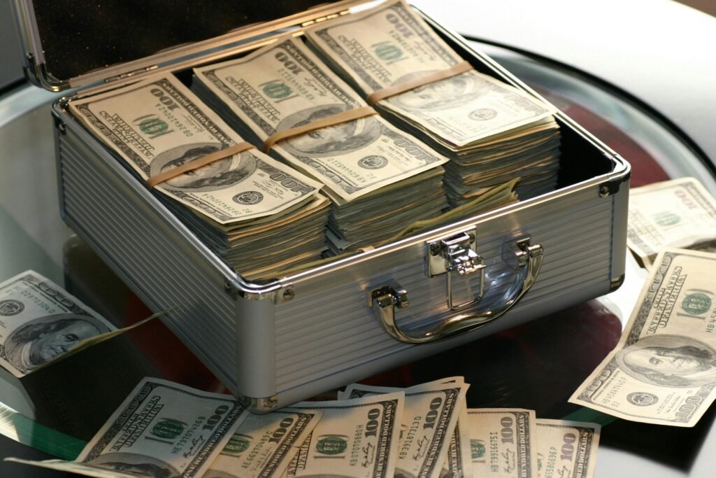 10 Smart Ways You Can Build Wealth In Today’s Economy: A Beginner’s Guide by Invest Smart Edge Team. 10 Open briefcase filled with stacks of hundred dollar bills on a glass table, representing wealth.
